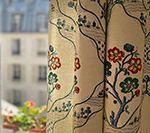 Curtains with floral pattern in front of a window overlooking a city building and flowers.