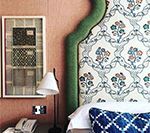Bed with patterned floral headboard, green trim, and a framed fabric sample on a pink wall.