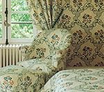 Chair and ottoman upholstered in patterned fabric, next to a window with matching curtains.
