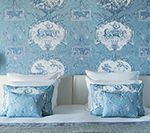 Two beds with blue and white patterned bedding against a matching wallpaper.