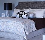 Bedroom with patterned headboard, white bedding, decorative pillows, and a black lamp.