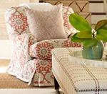 Upholstered armchair with red and white patterned fabric and a patterned pillow. A matching ottoman and plant are nearby.