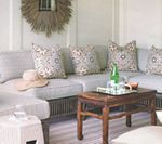 Cozy outdoor seating area with sectional sofa, decorative pillows, wooden coffee table, and straw sun hat.