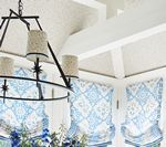 Chandelier above a table with blue and white patterned curtains in a bright white room.
