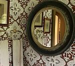 Round mirror on patterned wall, reflecting a doorway and framed artwork.