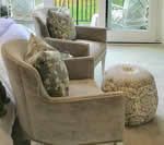 Two beige armchairs with patterned pillows and a decorative ottoman in a living room.