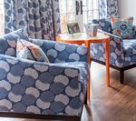 Blue patterned furniture in a room with a round orange table, wooden floor and floral curtains.