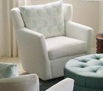 White upholstered swivel armchair with patterned pillow, near a teal ottoman.