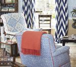 Cozy living room with blue patterned chairs, orange throw, chevron curtains, and a dark wooden table.