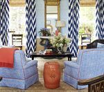 Living room with blue chairs, orange accent stool, chevron curtains, and a coffee table.