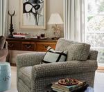 Cozy living room with patterned armchair, antique wooden sideboard, artwork, and side table.