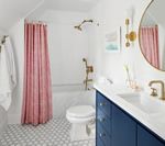 Bathroom with pink shower curtain, blue vanity, gold fixtures, and patterned floor.