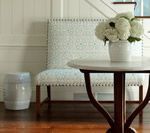 A white floral arrangement on a round table, a patterned chair, and a small ceramic stool in a wood-floored entryway.