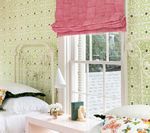 Bedroom with light green wallpaper, pink window shade, white bed and nightstand.
