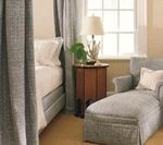 Bedroom with draped bed, chaise lounge, side table with lamp, and window. Soft, neutral color palette.