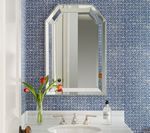 Bathroom with blue patterned wallpaper, octagonal mirror, white sink, and flowers in a vase.