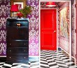 Hallway with purple patterned wallpaper, black dresser, and red door. Black and white striped floor.