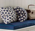 Two patterned pillows and a satchel on a navy bench with blue piping, against a white panel wall.