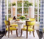 Yellow chairs around a white table in a light-filled dining room with tall windows and blue patterned curtains.