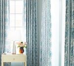 Window with blue patterned curtains, a side table with a vase of flowers.