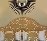 Gold patterned headboard with white pillows, sunburst mirror.