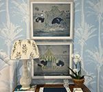 Two framed bird prints above a table with a lamp, orchid, and patterned wallpaper.