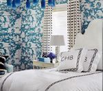 Bedroom with white bed, patterned wallpaper, blue chandelier, and monogrammed pillows.