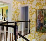 Staircase with black railing, white balusters, and floral yellow wallpaper; painting on the wall.