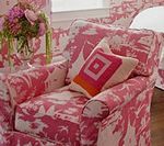 Pink and white patterned armchair with a decorative pillow, near flowers.