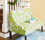 Lime green patterned loveseat with dark legs, against a white stairwell, and a blue rug.