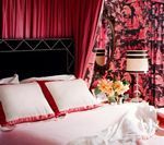 Bedroom with pink curtains, black headboard, floral wallpaper, and white bedding with red trim.