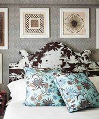 Bed with patterned headboard, floral pillows, framed art on gray wallpaper.