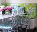 Dining area with white table, clear chairs, and green patterned bench seating. Flowers sit on the table.