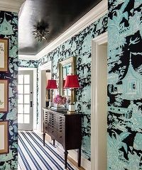 Hallway with black ceiling, patterned wallpaper, dark wood cabinet, red lamps, and striped rug.