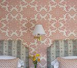 Pink patterned wallpaper, two floral headboards, and a lamp with a small bouquet of yellow flowers.
