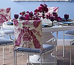 White dining table set with chairs, floral chair covers, purple accents, and blue walls.