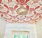 Red patterned wallpaper ceiling with a chandelier and white walls.