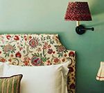 Floral headboard with white pillows, green wall, patterned lampshade and wall-mounted lamp.