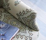 Close-up of a patterned sofa arm with a book lying next to it; beige and green.