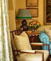 Cozy living room corner with floral chair, teal couch, lamp, and framed art against yellow walls.