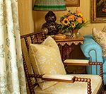 Cozy room with antique furniture: patterned chair, turquoise sofa, side table with flowers, and green lampshade.