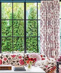 Window with floral curtains and cushions; dog on seat, greenery outside.