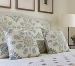 Bed with patterned pillows and headboard in a light blue and beige color scheme. Artwork on the wall above.