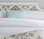 White bed with light blue pillow and patterned headboard.