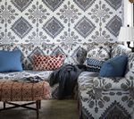 Living room with patterned wallpaper and sofa, blue pillows, patterned ottoman.