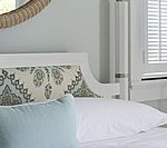 White bed with light blue and patterned pillows, and a window with blinds.