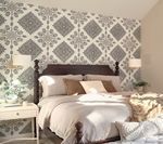 Bedroom with bed against a patterned gray and white wallpaper wall, nightstands, and lamps.
