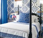 Bedroom with patterned blue wallpaper, white bedding, and black four-poster bed.