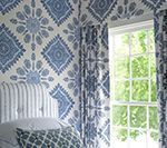 Bedroom with blue patterned wallpaper, curtains, and bedding, featuring a window with a view of greenery.