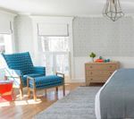 Bedroom with a blue patterned chair, orange side table, light wood dresser, and gray rug.